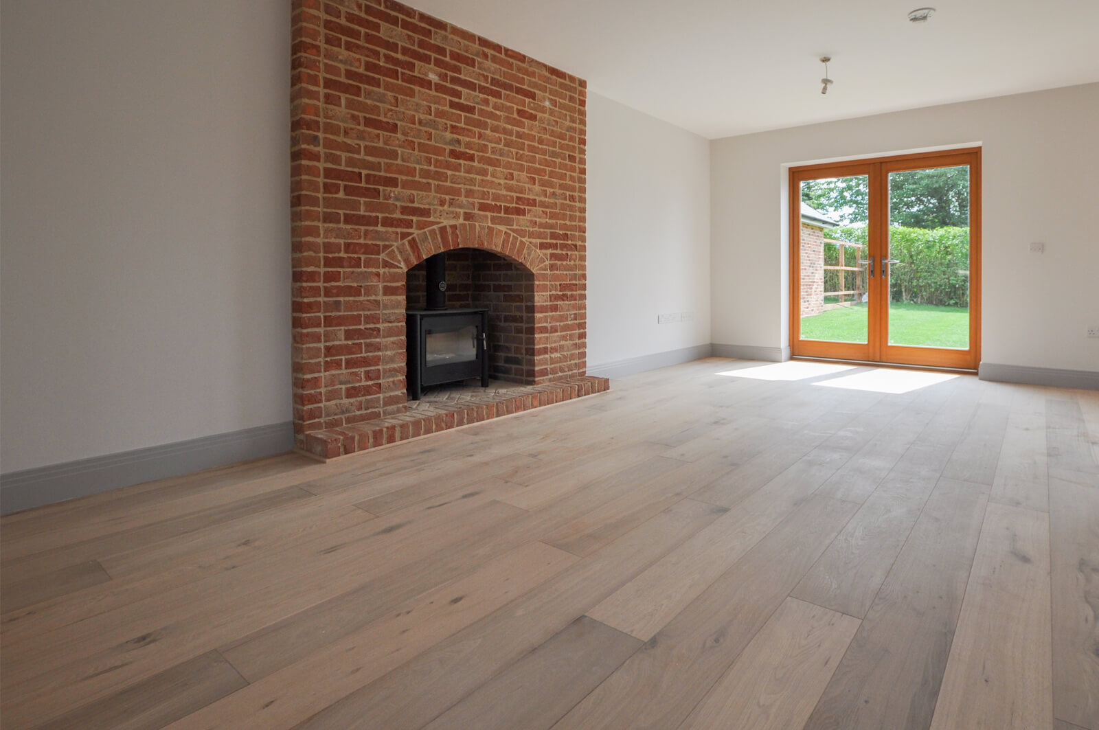 Interior view of room with a brickwork fireplace and glass door to the back garden.