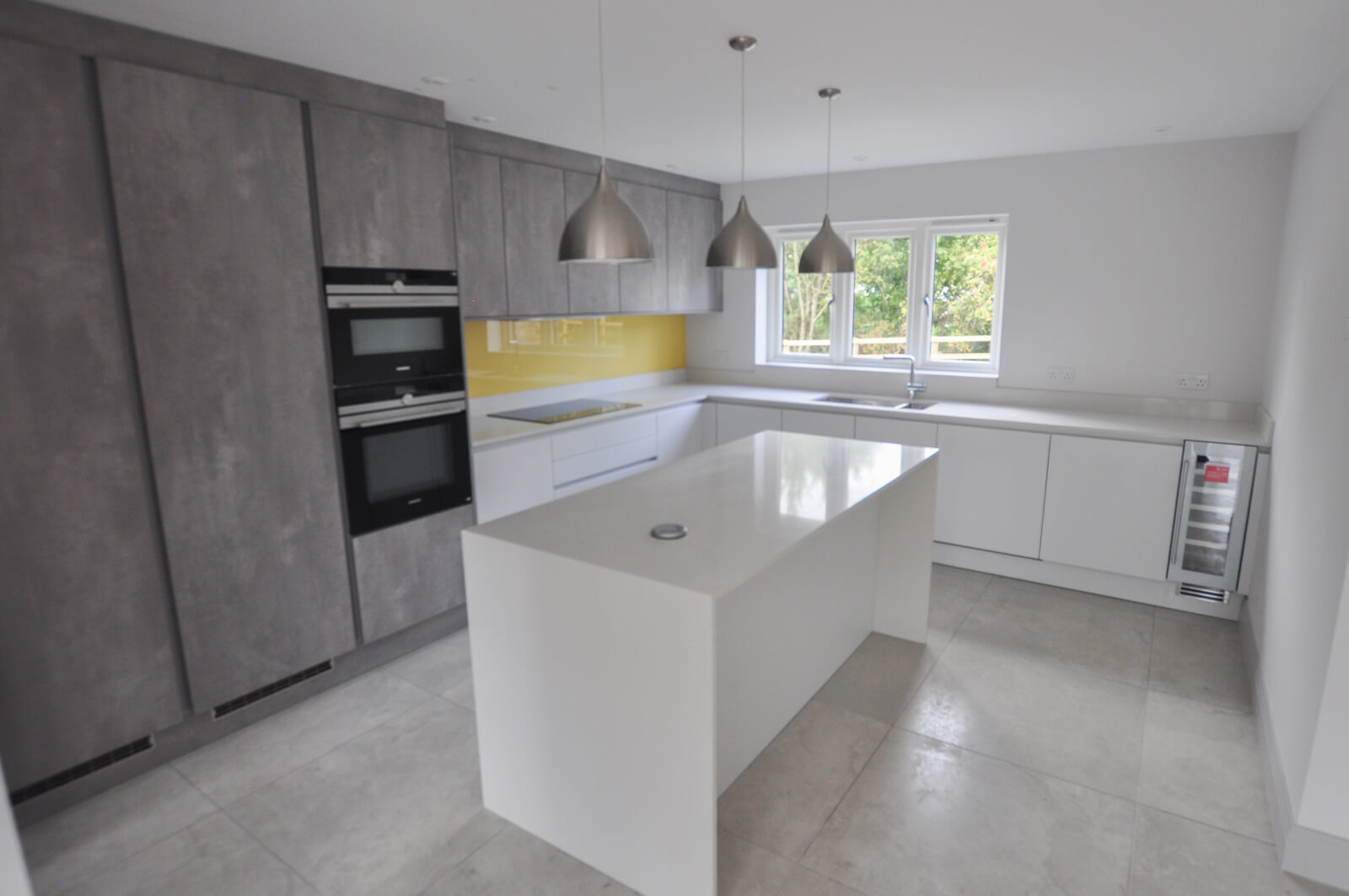 Kitchen with center white table and 3 steel lights above.