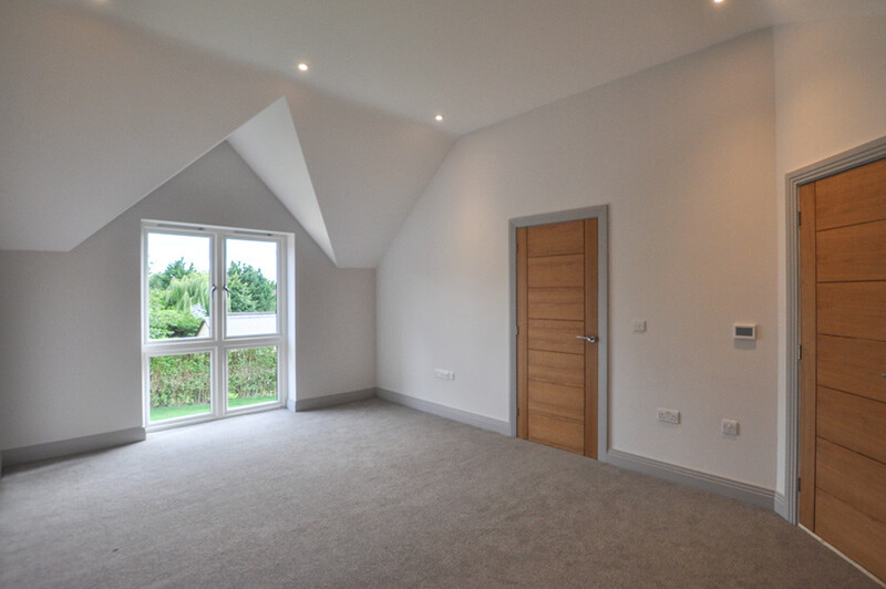 Spacious bedroom with white walls, warm grey carpet, large window opening over back garden.