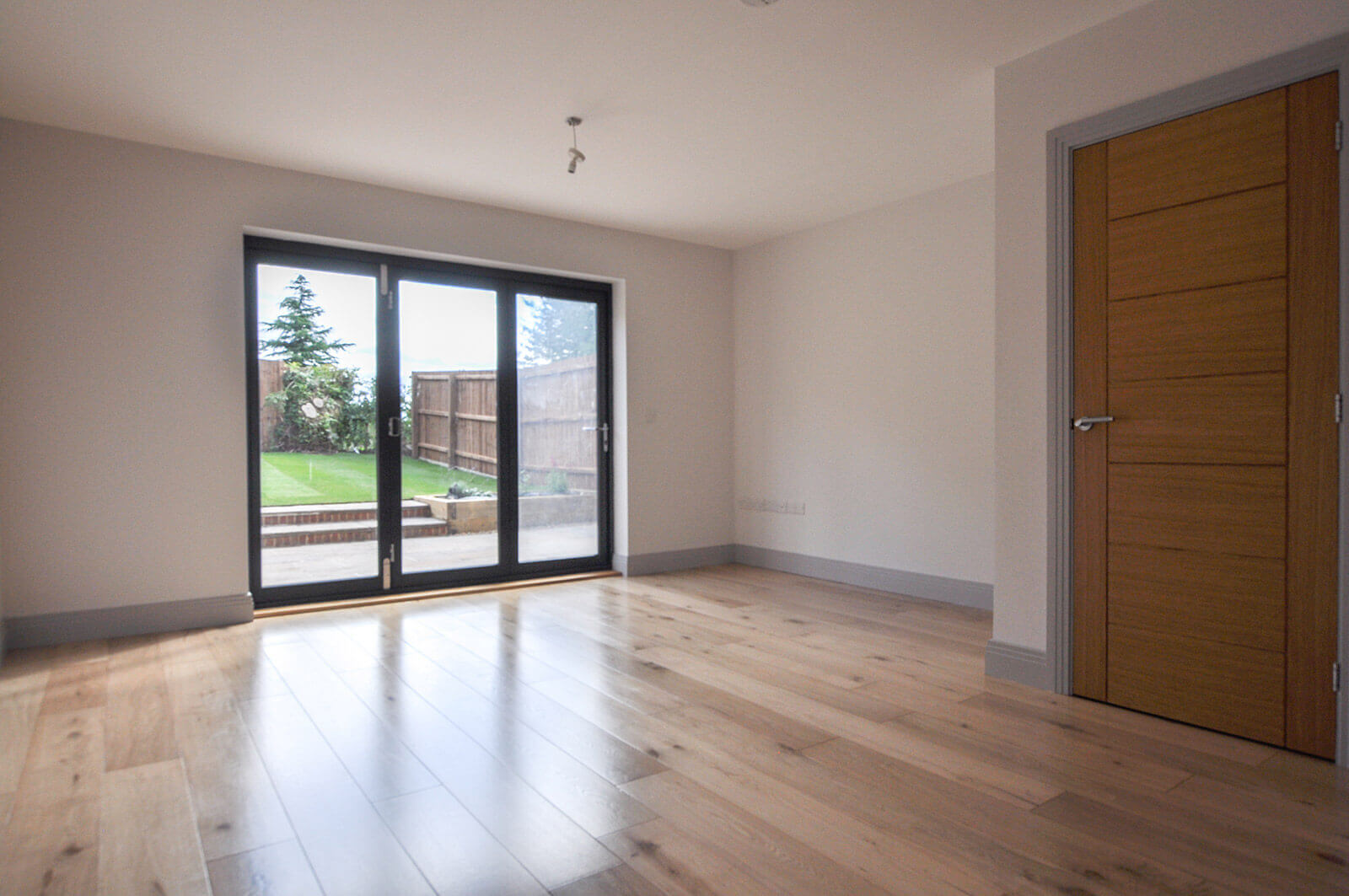 Living room with light hard wood floors and glass bi-fold doors leading to back garden.