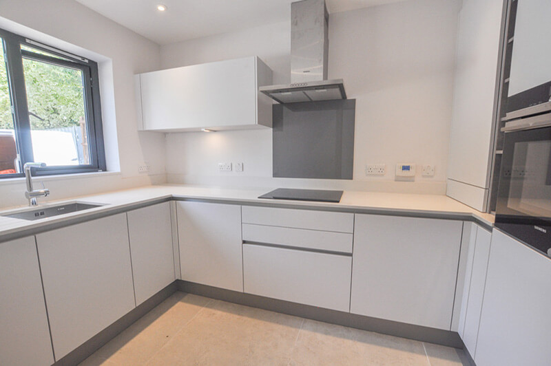 Bright white square kitchen with sink to the left, hob in the middle and oven to the right.