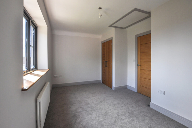 Bedroom with white walls, warm grey carpet and in built wardrobe.