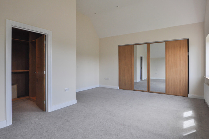 Spacious bedroom with white walls, grey carpet and in-built wardrobe.