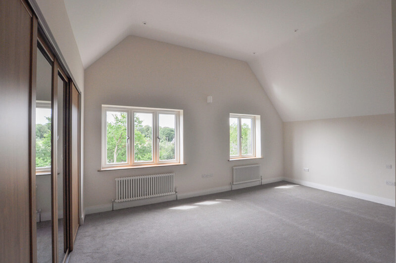 Spacious top floor bedroom with white walls, grey carpet and large in-built wardrobe.