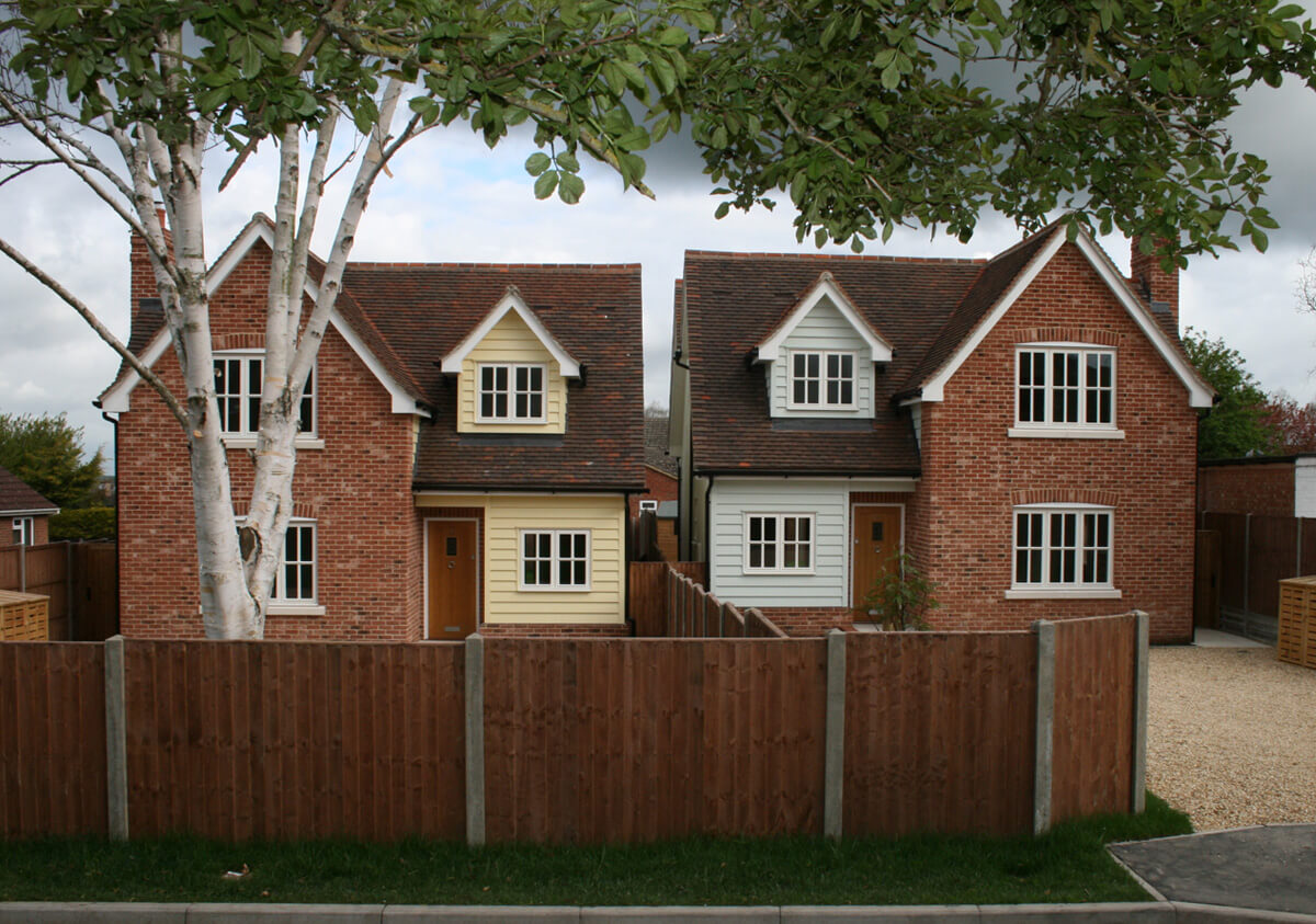 Front view of two detached houses both with fence lined driveways.