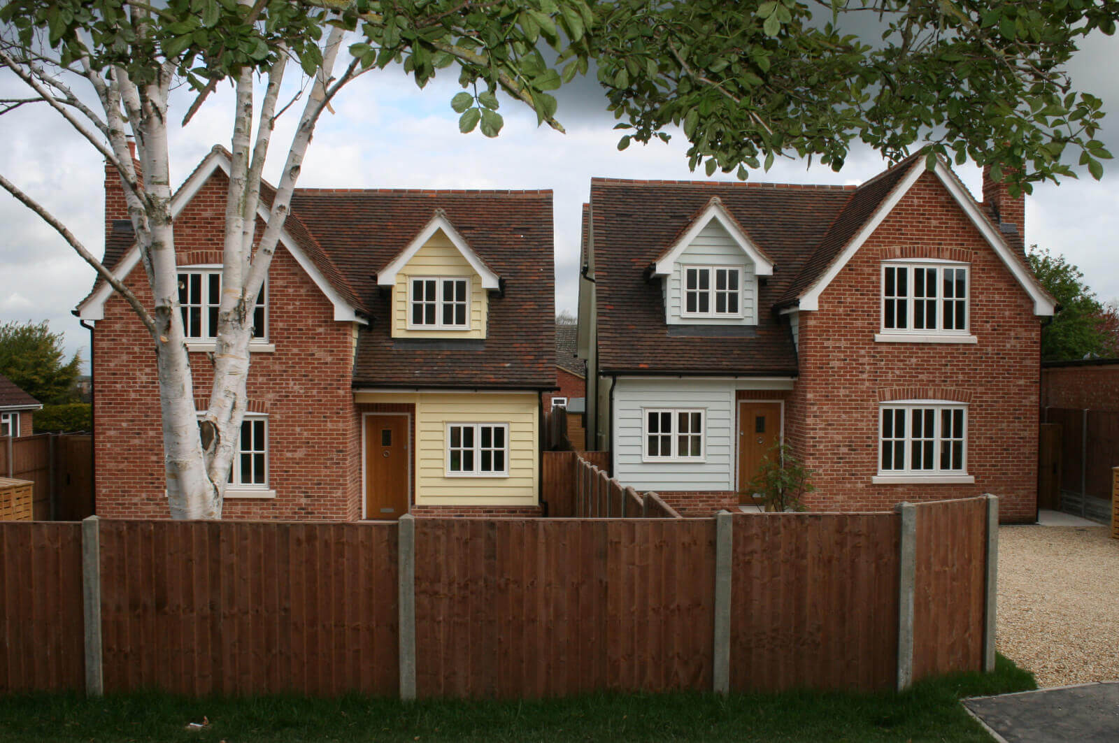 Front view of two detached houses both with fence lined driveways.