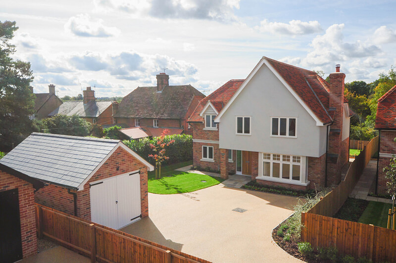 Raised front view of house showing wide driveway, front garden and garage to the side.