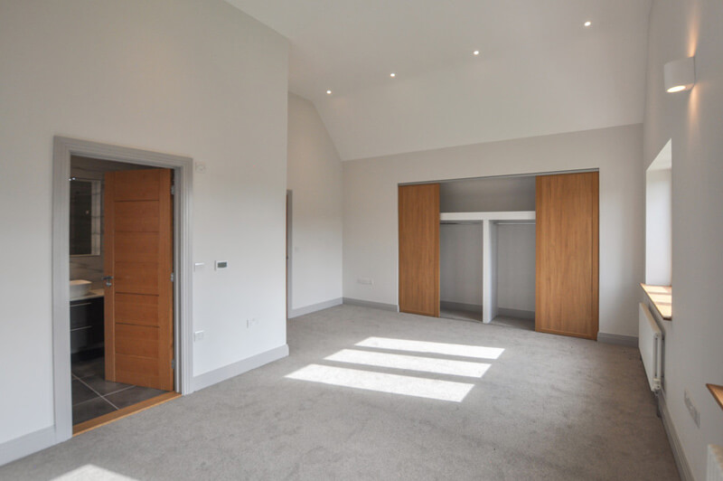 Bedroom with white walls, grey carpet and open door to en-suite bathroom.