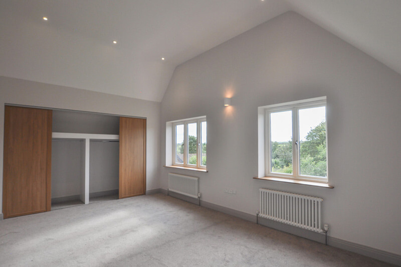 Spacious bedroom with white walls, grey carpet and large in-built wardrobe.