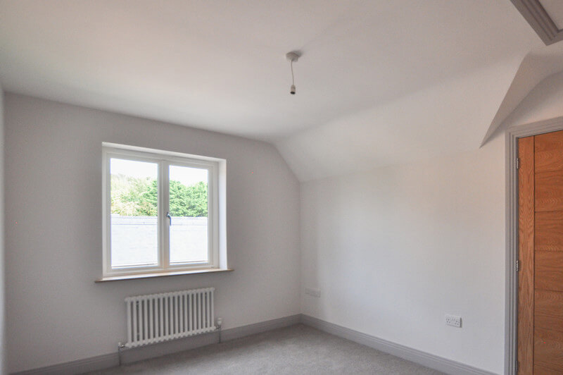 Spacious bedroom with white walls and wooden door.